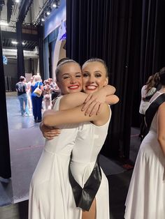 two women hugging each other in front of a stage with people standing around and looking at the camera