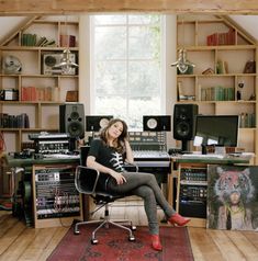 a woman sitting in a chair next to a desk full of sound equipment and books