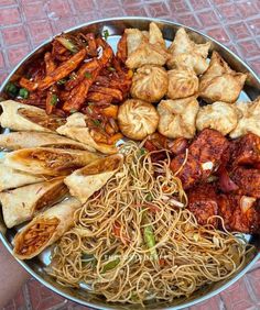 a large metal bowl filled with lots of different types of food on top of a red brick floor