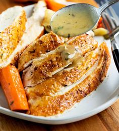 a white plate topped with meat and carrots next to gravy on top of bread