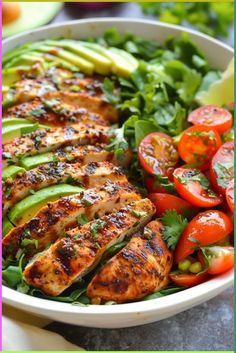 a white bowl filled with chicken, tomatoes and lettuce next to sliced cucumbers