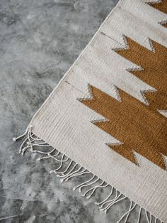 a brown and white rug with tassels on the bottom is laying on concrete