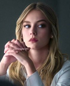 a woman with long blonde hair and blue eyes looking at the camera while wearing a white shirt