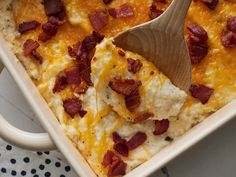 a casserole dish with cheese and bacon on top, next to a wooden spoon