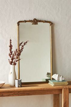 a mirror sitting on top of a wooden table next to a vase filled with flowers