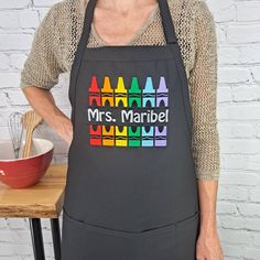 a woman wearing an apron that has crayons on it and the words mrs marbrel written in large letters