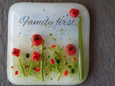 a glass plate with red and green flowers on it that says family first in the center