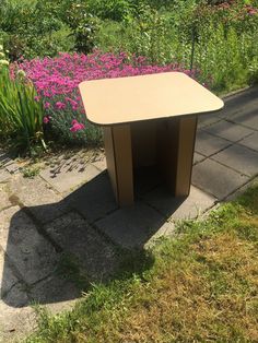 a small table sitting in the middle of a garden with pink flowers behind it and green grass