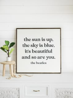 a white dresser with a plant and a framed quote on the wall above it that says he sun is up, the sky is blue, it's beautiful and so are you