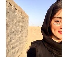 a woman wearing a black hoodie standing next to a stone wall