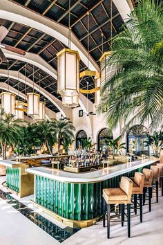 an indoor bar with lots of chairs and palm trees in the background, surrounded by tall ceilings