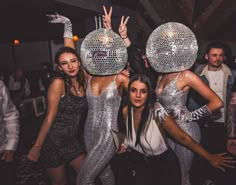 three women in silver dresses posing for the camera with disco balls on their heads at a party