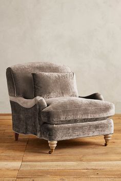 a gray chair sitting on top of a hard wood floor next to a white wall