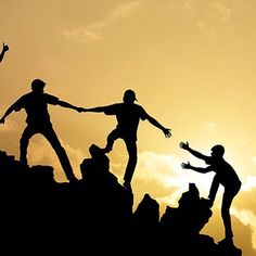 four people are standing on top of a mountain and reaching for the sky with their hands