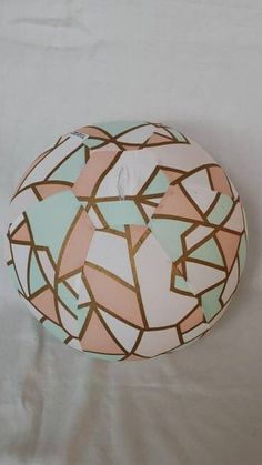 a round object with geometric designs on it sitting on a white sheeted surface in front of a wall