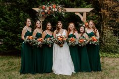 a group of women standing next to each other in front of a wooden arch with flowers