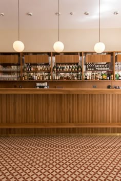 an empty bar with lots of bottles on the shelves and lights hanging above it in a restaurant