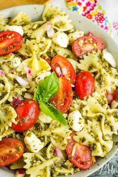 a bowl filled with pasta, tomatoes and pesto on top of a wooden table