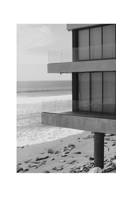 a black and white photo of a building on the beach with water in the background