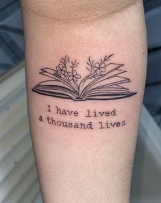 a tattoo with an open book and flowers on it that says i have lived a thousand lives