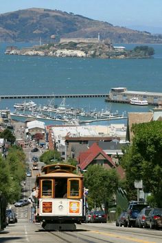 a trolley car traveling down a street next to the ocean with boats in the water