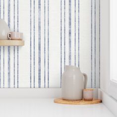 two white vases are sitting on a shelf in front of a striped wallpaper