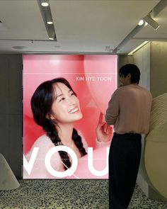 a man standing next to a woman in front of a large screen with the words you on it