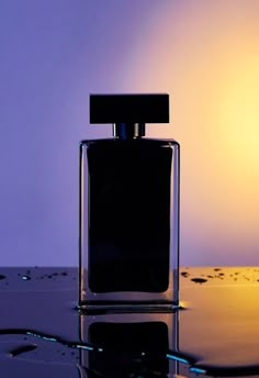 a bottle of perfume sitting on top of a table next to a light bulb in the background