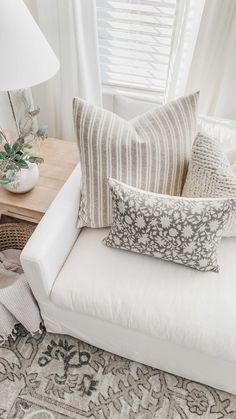 a white couch with pillows on top of it next to a lamp and window sill