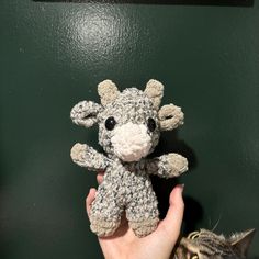 a hand holding a small crocheted stuffed animal in front of a green wall