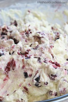 a mixing bowl filled with white batter and blueberry toppings, next to a red spatula