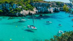 several sailboats are anchored in the clear blue water near rocky coastlines and cliffs