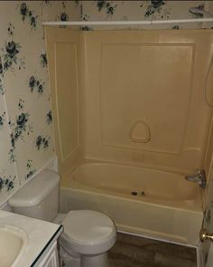 a bathroom with a toilet, sink and bathtub in the corner next to a wallpapered wall