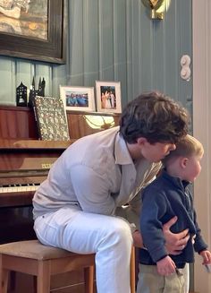 a man kneeling down next to a little boy in front of a piano and looking at something