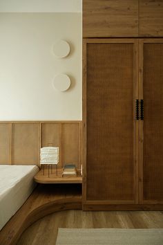 a bed sitting next to a wooden cabinet in a room with white walls and wood flooring