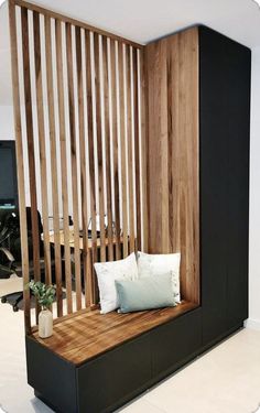 a wooden bench with pillows on it in front of a wall divider that is made out of wood slats