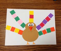 a turkey made out of colored paper sitting on top of a wooden table next to crayons