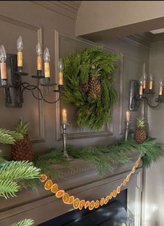 a mantel decorated with pine cones and greenery, candles and garland on the mantle