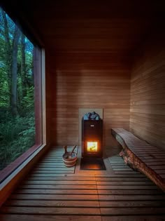 a wooden room with two benches and a fire place in the center, surrounded by trees