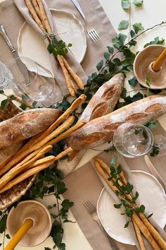 a table topped with bread and plates covered in leaves next to utensils on top of napkins