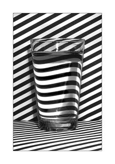 a black and white photo of a glass with water in it on a striped surface