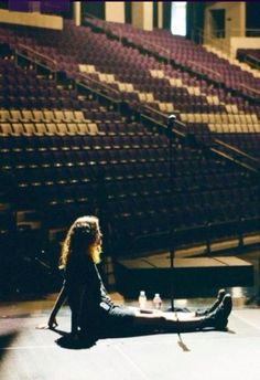 a woman sitting on the floor in front of an empty stage with a microphone next to her