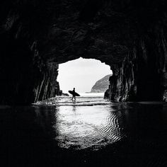 a man holding a surfboard standing in the middle of a dark cave with water