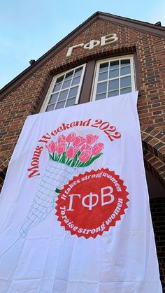 a banner hanging from the side of a brick building with flowers in vases on it