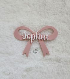 a pink ribbon with the word sophia on it sitting on a white blanket