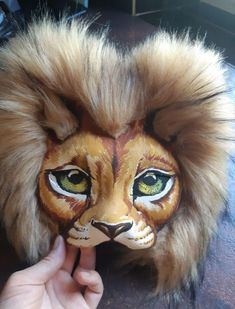 a lion mask is being held up by someone's hand with the face painted on it