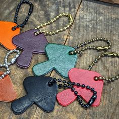 four different colored leather dog tags on a wooden table with beads and chains hanging from them