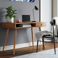 a desk with a laptop on it in front of a chair and wall mounted painting