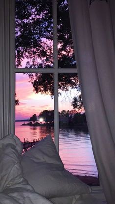 an open window overlooking the water at sunset or dawn with white sheets and pillows on it