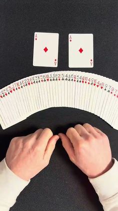 two hands are holding playing cards on a table